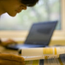 Foto van een jongen die in een schoolboek kijkt met een laptop op de achtergrond