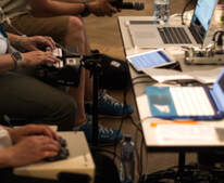 Foto van tafel met laptops waaraan personen zitten met een notitietoestel op hun  schoot