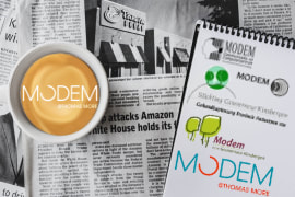 Foto met een krant op de achtergrond. Hierop staat een tas cappuccino met het logo van Modem en een notitieboek met oude logo's van Modem. 