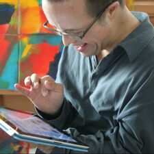 Foto van volwassen man met het syndroom van Down die een tablet vast heeft en er naar kijkt.
